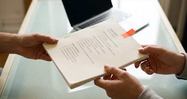 Zwei Hände übergeben ein ausgedrucktes Dokument mit Checkliste